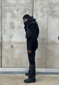 Black padded vest over a ribbed black turtleneck, teamed with black jeans and knee-high slouchy black boots. Grey sunglasses finish off the outfit.