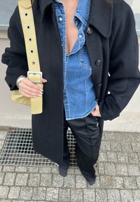 Black wool coat, denim shirt underneath, black trousers, yellow crossbody bag with a rectangular buckle, and light grey shoes.