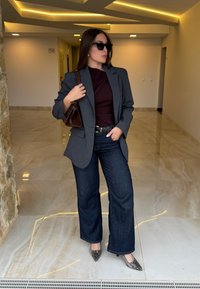 Blazer à carreaux gris, haut bordeaux, jean flare en denim foncé et talons à imprimé serpent. Sac à main marron et lunettes de soleil complètent le look.