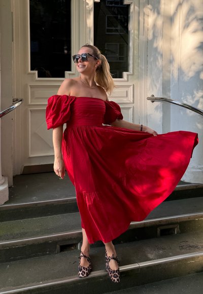 Vestido rojo de un solo hombro con mangas abullonadas, falda en capas y textura suave. Se lleva con zapatos planos de estampado de leopardo, de pie en escaleras de piedra.