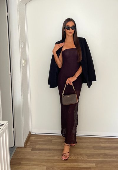 Vestido burdeos ajustado sin tirantes con tejido texturizado, combinado con una chaqueta negra y un pequeño bolso marrón con cadena dorada. Gafas de sol negras.