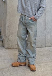 Jeans in denim chiaro con vestibilità rilassata, abbinati a un cardigan grigio con bottoni. Scarpe zoccolo color cuoio con suola strutturata completano l'outfit.