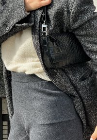Bolso negro de piel con estampado de cocodrilo y clip plateado, combinado con un abrigo gris texturizado, suéter blanco crema y pantalones gris a juego.