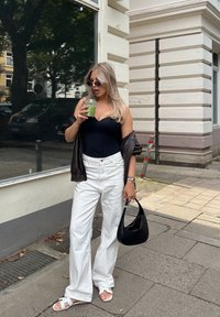 Fekete, testhezálló overál; túlméretezett barna dzseki; fehér bő nadrág; fehér szandál; fekete kézitáska; zöld ital; városi környezet.