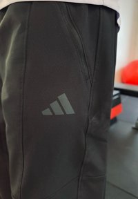 Fekete sportnadrág szürke Adidas logóval a combon, sima textúrájú, cipzáras zsebbel és testre szabott szabással.