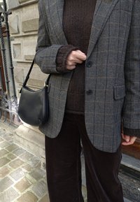 Grå hundetannsblazer med to knapper, brun strikkegenser og brune kordfløyelsbukser. Svart skulderveske i skinn med buet form.