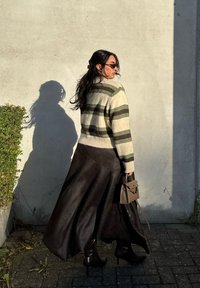 Prúžkovaný pletený sveter v krémovej, zelenej a hnedej farbe; dlhá hnedá kožená sukňa; drží malú hnedú kabelku; nosí tmavé slnečné okuliare a čižmy na podpätku.