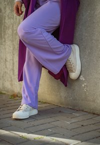 Μωβ φαρδιά παντελόνια συνδυασμένα με λευκά αθλητικά παπούτσια. Τα παπούτσια διαθέτουν τρύπες και υφή στη σόλα, ενώ τα παντελόνια έχουν λεία υφή.