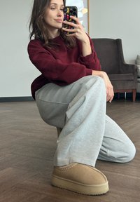 Beige ankelstøvler med tekstureret overflade og synlige sømme, båret med lysegrå joggingbukser og en bordeaux sweatshirt. Glat gulv nedenunder.