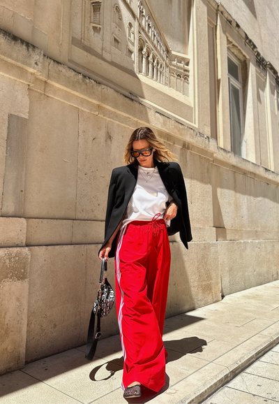 Pantalones rojos de pierna ancha con rayas blancas, combinados con una chaqueta negra y una camiseta blanca. Los accesorios incluyen un pequeño bolso estampado.