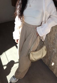 Pantalones de pierna ancha a rayas beige y azul marino, blusa ajustada blanca, chaqueta ligera color crema y un pequeño bolso metálico dorado. Zapatillas plateadas.