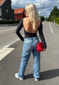 Body negro de manga larga con espalda descubierta, jeans de tiro alto azul claro y un bolso rojo. Zapatillas grises completan el conjunto.