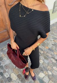 Svart ribbet off-shoulder topp, svarte tettsittende bukser, burgunder teksturert håndveske med flettede håndtak, og mørke flate sko med subtilt design.