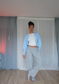Hellblaues Cardigan über einem weißen Cropped-Top, graue weite Hose und graue Sneakers; glatte Texturen, sanfte Farben und lockerer Schnitt.