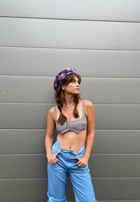 Top cropped cinza xadrez com botões, combinado com calças largas azuis claras. A modelo usa uma boina xadrez rosa e tem cabelo trançado.