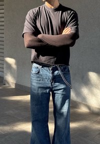 Μαύρη κοντομάνικη μπλούζα, μπλε τζιν και μια αλυσίδα ως αξεσουάρ. Το ύφασμα φαίνεται μαλακό, με άνετο σχέδιο και χαλαρή εφαρμογή.