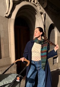 Zils mētelis, balts tops ar baltiem punktiņiem un platām džinsa biksēm. Krāsaina šalle ar zaļām, zilām un sarkanām svītrām. Brūna ratiņu roktura daļa ar uzlīmi.