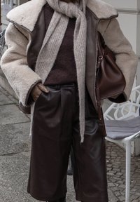 Shorts en cuir marron associés à un pull marron, un manteau en peau lainée crème et une écharpe gris clair. Comprend un sac en cuir marron. Look texturé et superposé.