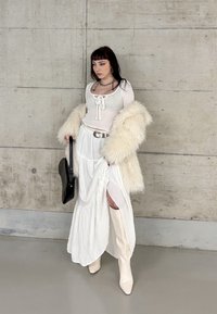 Camisola branca de mangas longas com detalhe em rendado, sobreposta a uma saia branca com fenda lateral, combinada com botas brancas até ao joelho e um casaco fofinho. Mala preta.