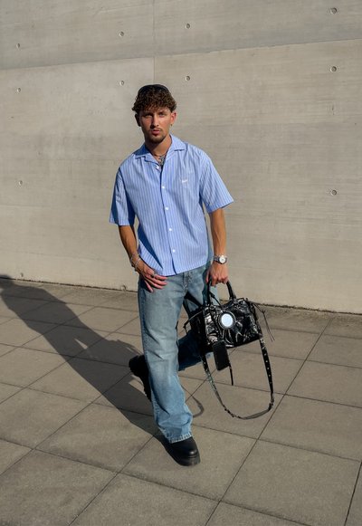 Camisa de rayas azul claro de manga corta, jeans de denim holgados y zapatos de plataforma negros. Bolso negro con detalle circular y asas.