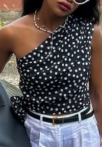 Μαύρη, μονόχοντρη μπλούζα με άσπρες πιτσιλιές; υφή υφάσματος; λεπτομέρεια με κόμπο στο πλάι; συνδυασμένη με μια μαύρη ζώνη και χαλαρά άσπρα παντελόνια.