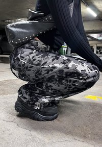 Black and grey floral-patterned wide-leg pants with a distressed texture, paired with chunky black platform sneakers and a studded black bag.