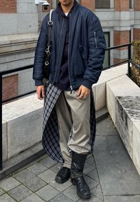 Ναυτικό bomber μπουφάν, γκρίζες παντελόνες με καρό από κάτω, μαύρες δερμάτινες μπότες, γκρι και μαύρες λεπτομέρειες με σχέδιο, και ασημένια δαχτυλίδια στα δάχτυλα.