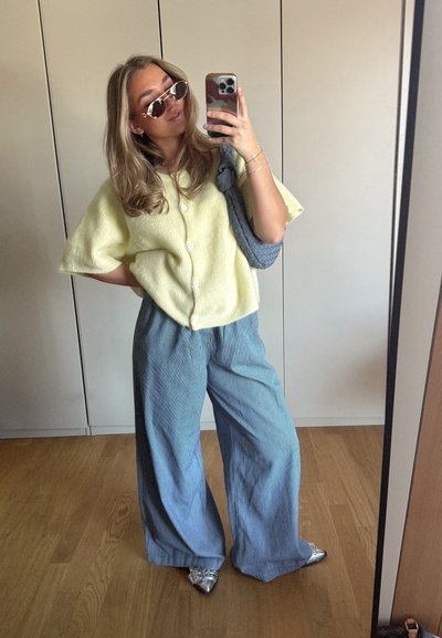 Cárdigan de punto amarillo claro, de corte oversize, con botones, combinado con pantalones anchos de rayas azul y blanca. Zapatos de punta plateada.