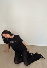 Black T-shirt with white text, black patterned leggings, and pointed black heels. The T-shirt features short sleeves, while the leggings have ruffled accents.