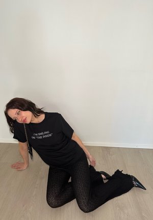 Camiseta negra con texto blanco, leggins negros con un patrón y tacones negros de punta. La camiseta tiene mangas cortas y los leggins tienen acentos con volantes.