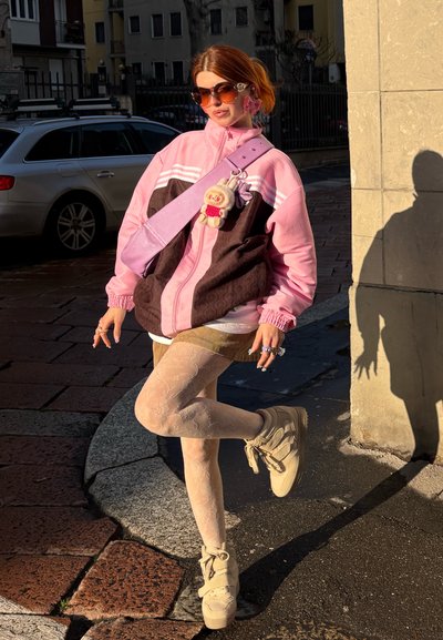 Chaqueta de gran tamaño en rosa y marrón con rayas blancas, superpuesta a una blusa blanca, pantalones cortos caqui y medias con estampado. Zapatillas de plataforma beige.