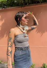 Γκρι τοπ χωρίς τιράντες με αλυσίδα, τζιν φούστα, μεγάλο περιδέραιο με πέρλες, δαντελωτό chokere, και έντονα κοσμήματα. Φόντο είναι ένας ροδάκινος τοίχος.