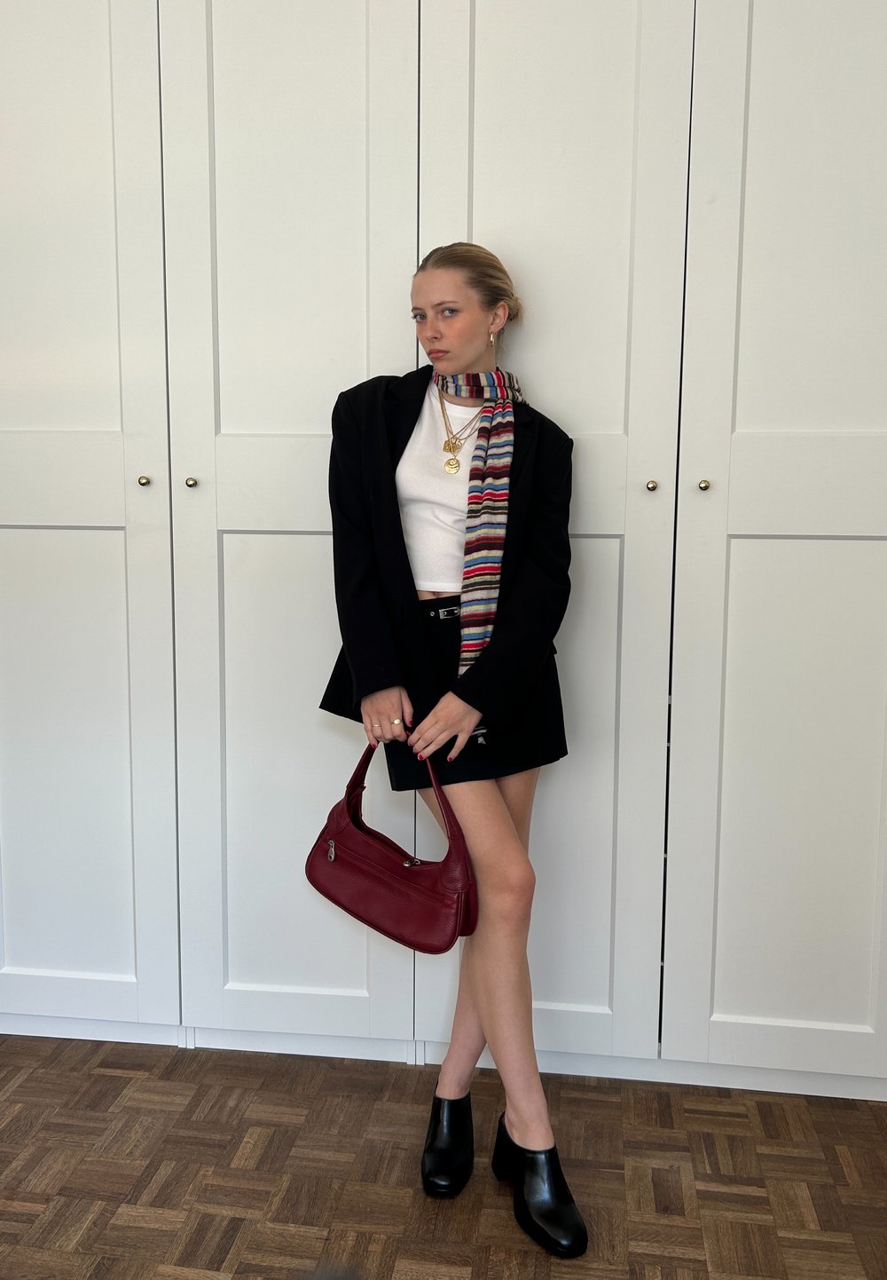 Black blazer over a white top, black mini skirt, red leather handbag, colourful striped scarf, and black heeled clogs.