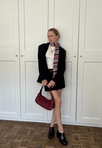 Black blazer over a white top, black mini skirt, red leather handbag, colourful striped scarf, and black heeled clogs.