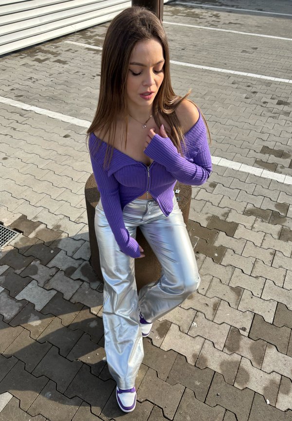 Top morado de tejido acanalado con escote asimétrico y cierre de cremallera, combinado con pantalones anchos plateados brillantes. Zapatillas blancas con acentos morados.