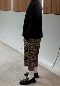 Černý blazer, kraťasy s leopardím potiskem, bílé ponožky a černé polobotky. Obsahuje detail kapsy a kontrastní textury materiálů.