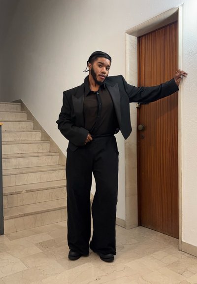 Chaqueta de traje negra ajustada sobre una camisa negra y pantalones de pierna ancha. Tejido suave, hombros estructurados y detalles mínimos.