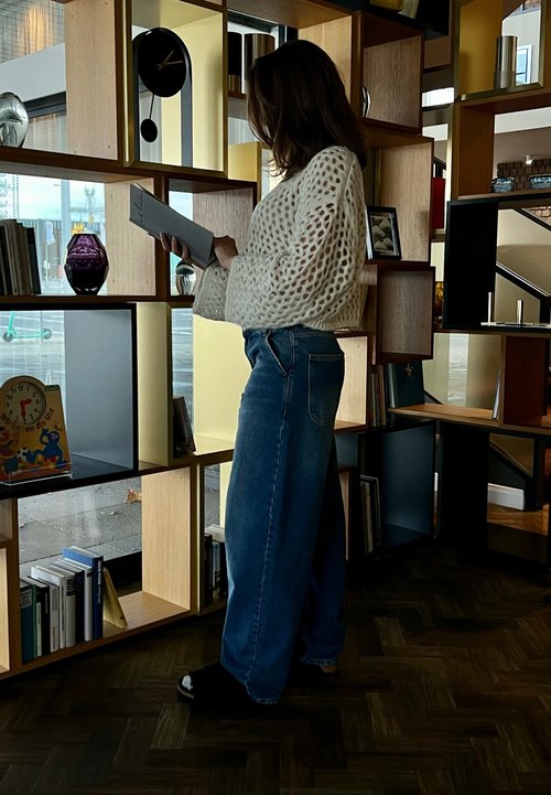 Pantalons cargo gris avec plusieurs poches, un gilet en polaire beige sur un crop top noir, et des chaussures de randonnée noires, disposés sur un banc en bois à l'extérieur.