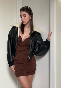 Svart läderbomberjacka med fårskinnskrage, tillsammans med en brun figurnära klänning som har samlad tyg och en dragkedja.