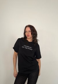 Black cotton t-shirt with short sleeves featuring white text that reads, "I'M SMILING ON 'THE INSIDE'" on the front.