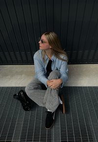 Καθημερινό ντύσιμο με ανοιχτό μπλε πουκάμισο και γκρι παντελόνι. Μαύρα αθλητικά παπούτσια με λευκές λεπτομέρειες και μια μαύρη τσάντα σε πλέγμα.