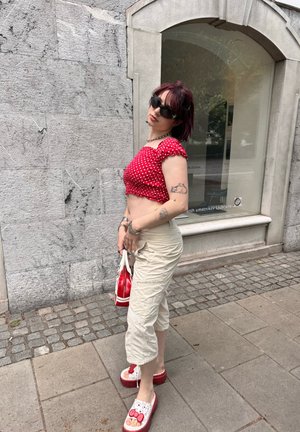 Top corto rojo con lunares, pantalones cargo beige, zuecos rojos y blancos con diseño de Hello Kitty, llevando un pequeño bolso rojo.