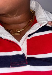 Polo à rayures rouges et blanches avec des accents marine, présentant un collier en chaîne dorée avec un design de maillons métalliques proéminents.