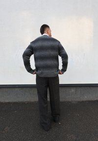 Pull rayé gris avec un ourlet côtelé, porté sur un pantalon à carreaux gris foncé, le tout conçu pour une coupe décontractée. Chaussures non visibles.