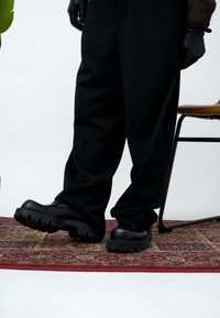 Czarne spodnie zestawione z masywnymi czarnymi butami o grubych podeszwach. Buty mają gładkie wykończenie z teksturowaną gumową podeszwą.