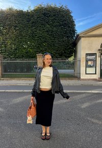 Zwarte midi-rok, witte cropped t-shirt, zwarte leren jas en geprinte ballerina's. Houden een geweven oranje handtas met een pluizig sleutelhanger.