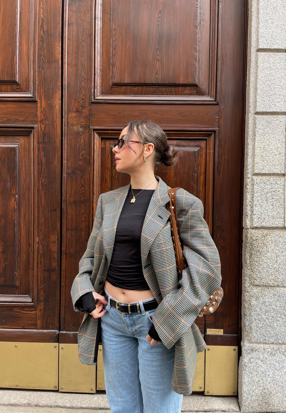 Blazer a scacchi con maniche oversize in tonalità tenui, abbinato a un top nero e jeans azzurri chiari, accessoriato con una borsa marrone.