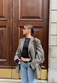 Blazer a scacchi con maniche oversize in tonalità tenui, abbinato a un top nero e jeans azzurri chiari, accessoriato con una borsa marrone.