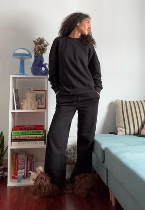 Sudadera negra y pantalones a juego con un corte relajado, que presentan detalles peludos marrones en los tobillos. Diseño sencillo sobre un fondo claro.