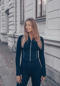 Top de manga longa azul-marinho com fecho, de design ajustado e comprimento cropped, emparelhado com leggings de cintura alta combinando, feitas de um tecido suave.